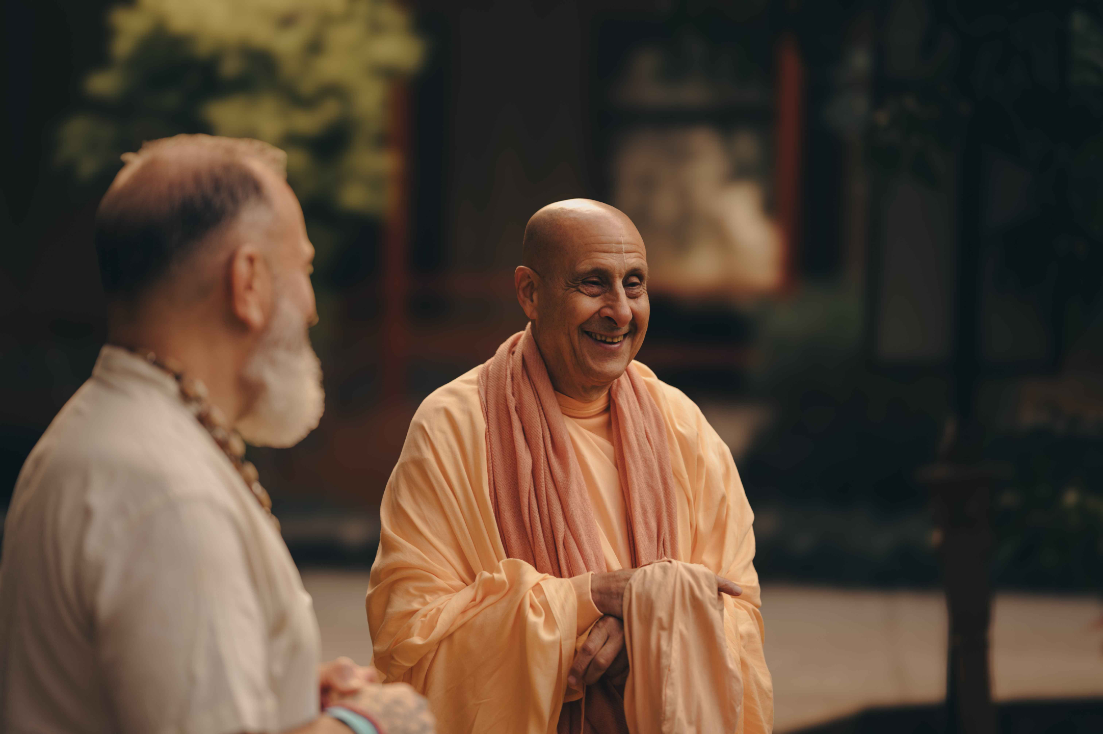 Smiling Hindu monk in traditional saffron robes engaged in conversation at Govardhan Eco Village, representing spiritual wisdom and devotional practice