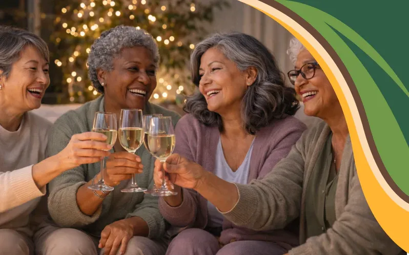 A diverse group of women aged 55 to 70 sit together in a cozy living room, raising glasses and laughing during a quiet New Year celebration. Soft lights and warm tones reflect a kinder New Year focused on connection, joy, and being present rather than excess or pressure.