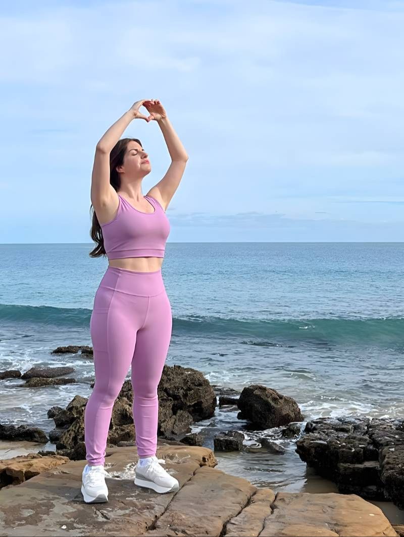 NARA, standing with eyes closed and hands in prayer, after a Qigong session with the ocean behind her. 