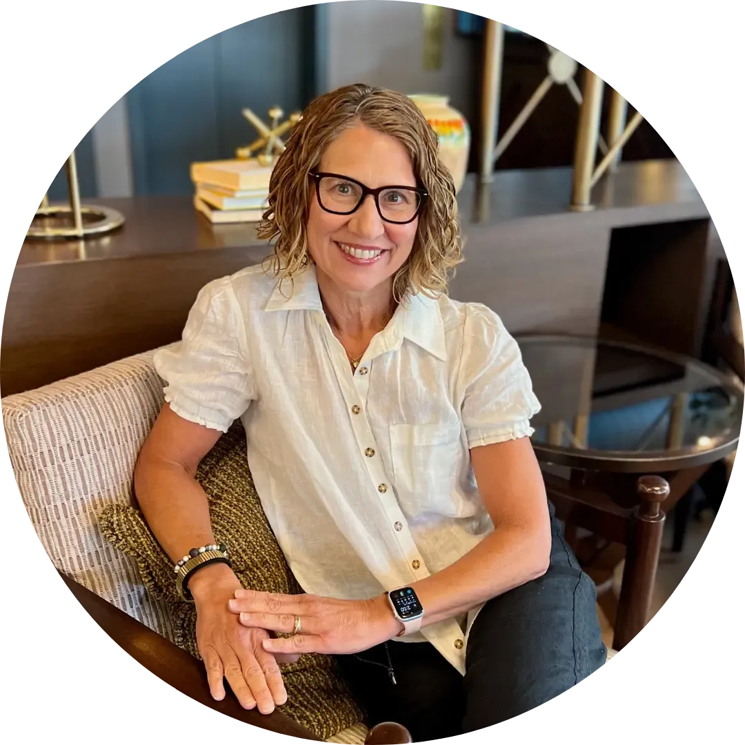Photo of intimacy coach heather england, a midlife woman with short brown wavy hair sitting on a chair smiling