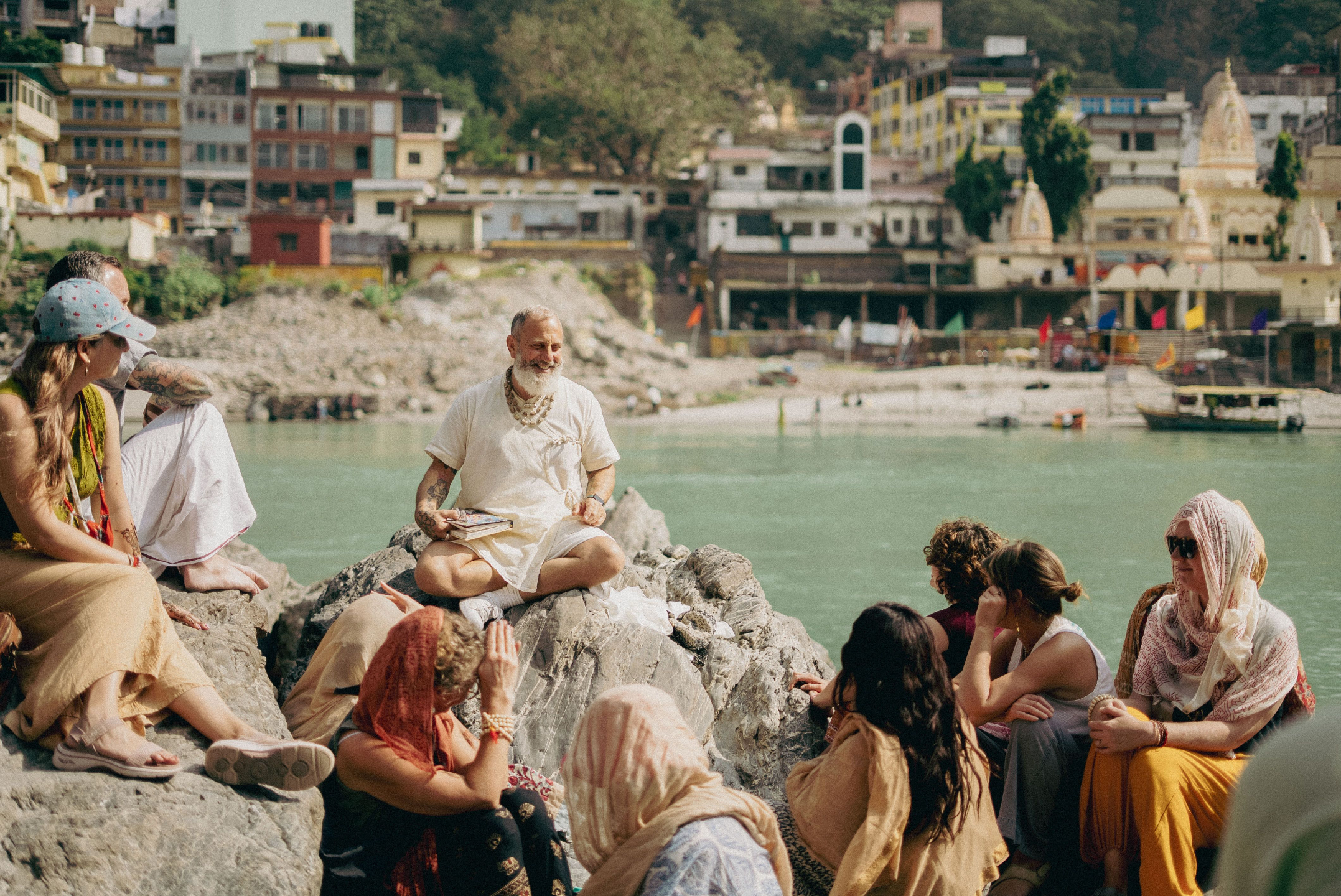 Raghunath Cappo teaching bhakti yoga philosophy to pilgrims beside the Ganges River in Rishikesh, India, during a guided spiritual pilgrimage.