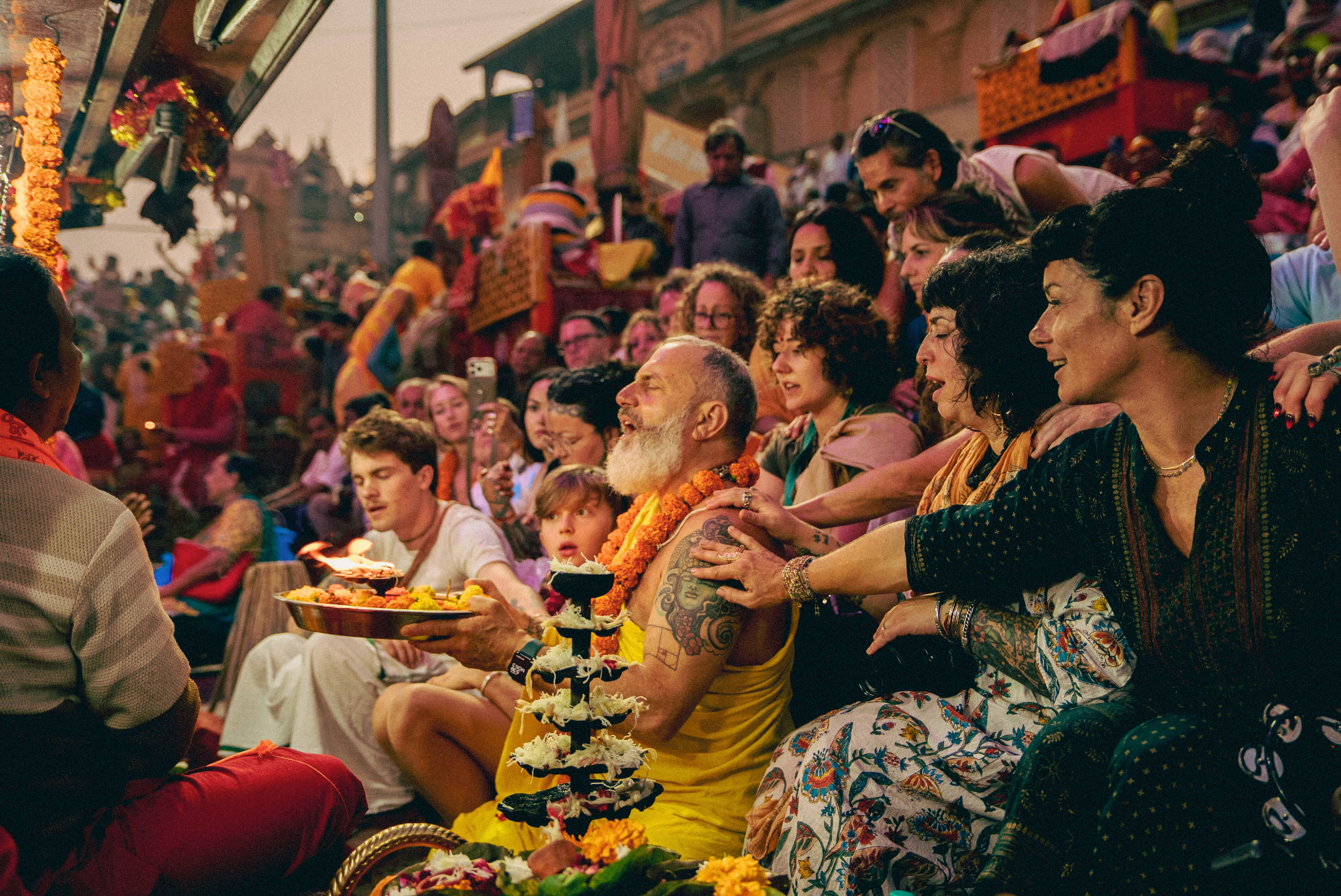 Group of pilgrims participating in a Ganga Aarti ceremony in India, gathered closely in devotion with lamps, flowers, and chanting along the river steps.