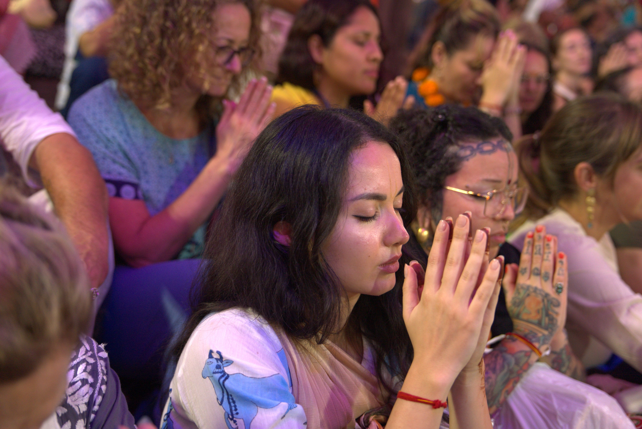 Pilgrims in prayer during a devotional kirtan gathering in India, hands folded in meditation and bhakti practice.