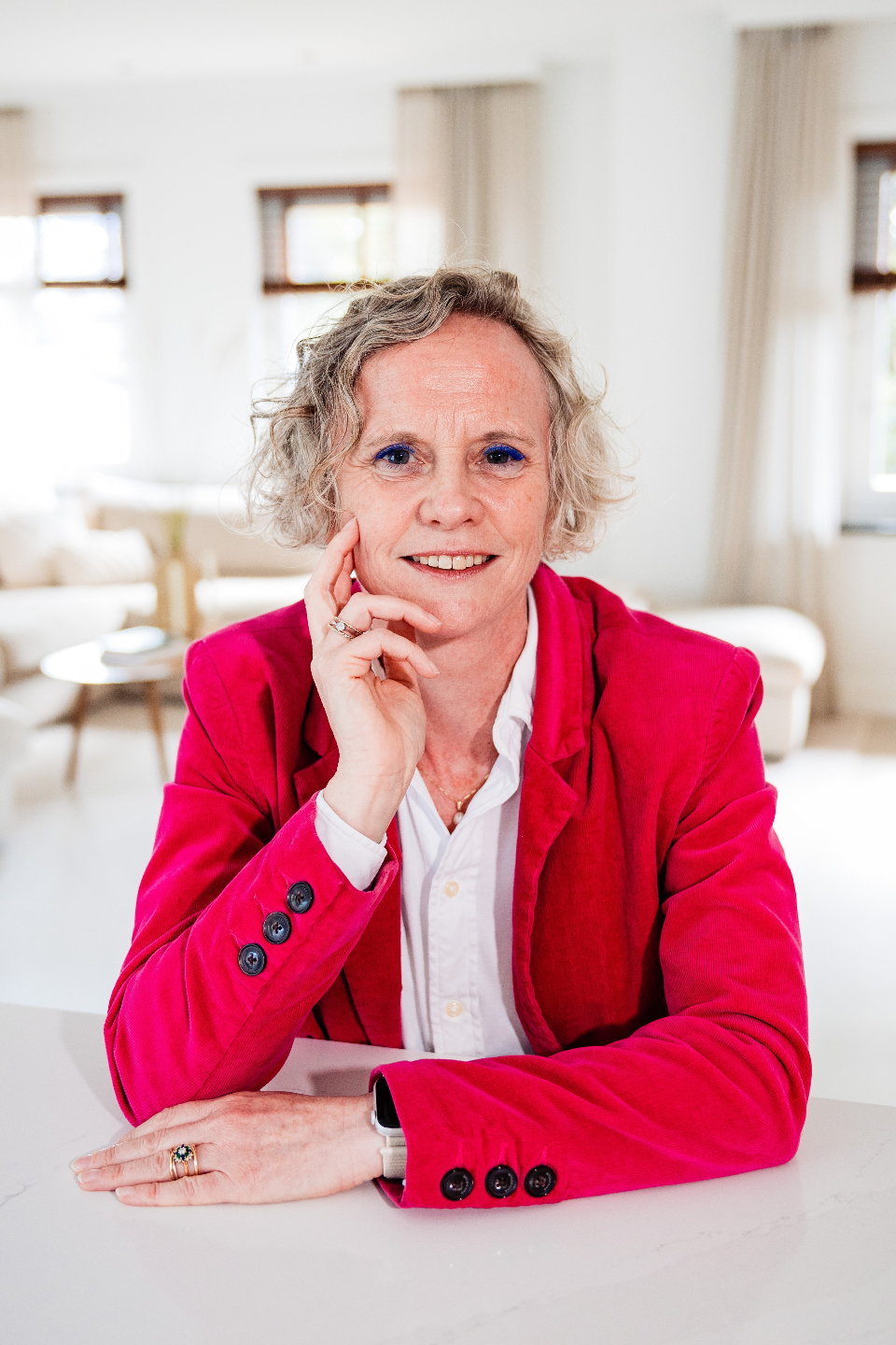 Jet wearing a white shirt and magenta blazer looking straight into camera, resting head in right hand