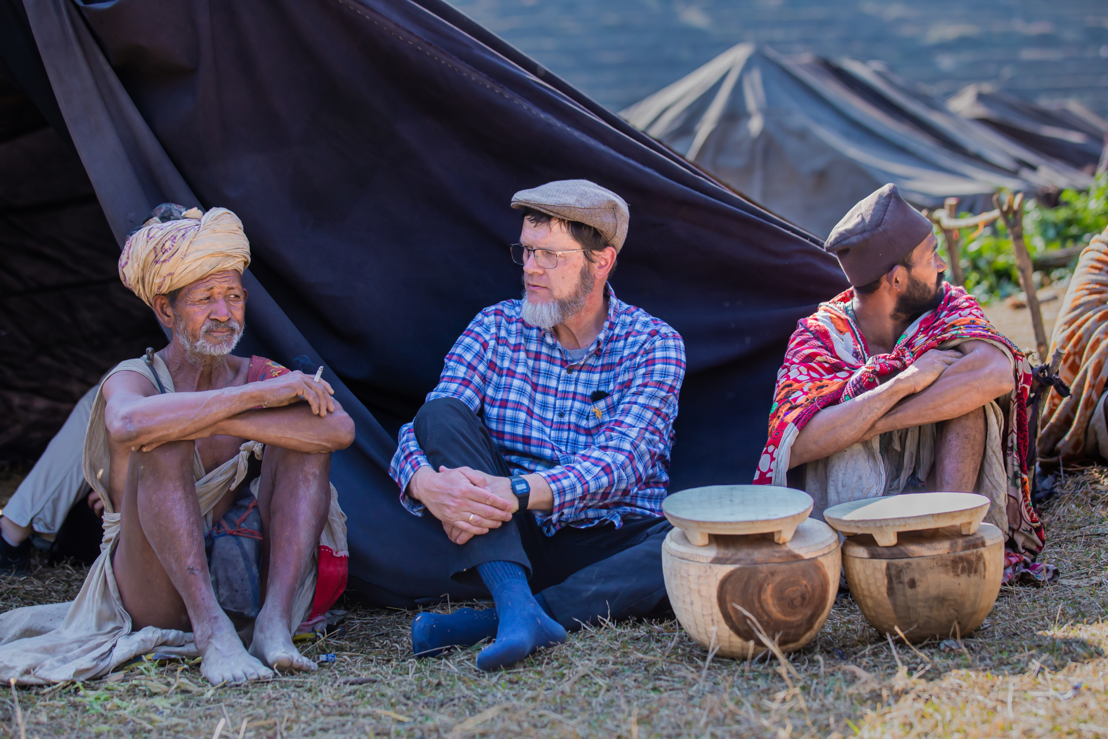 Ron sitting on the ground with two Raute elders in front of their tent during a conversation in their camp.