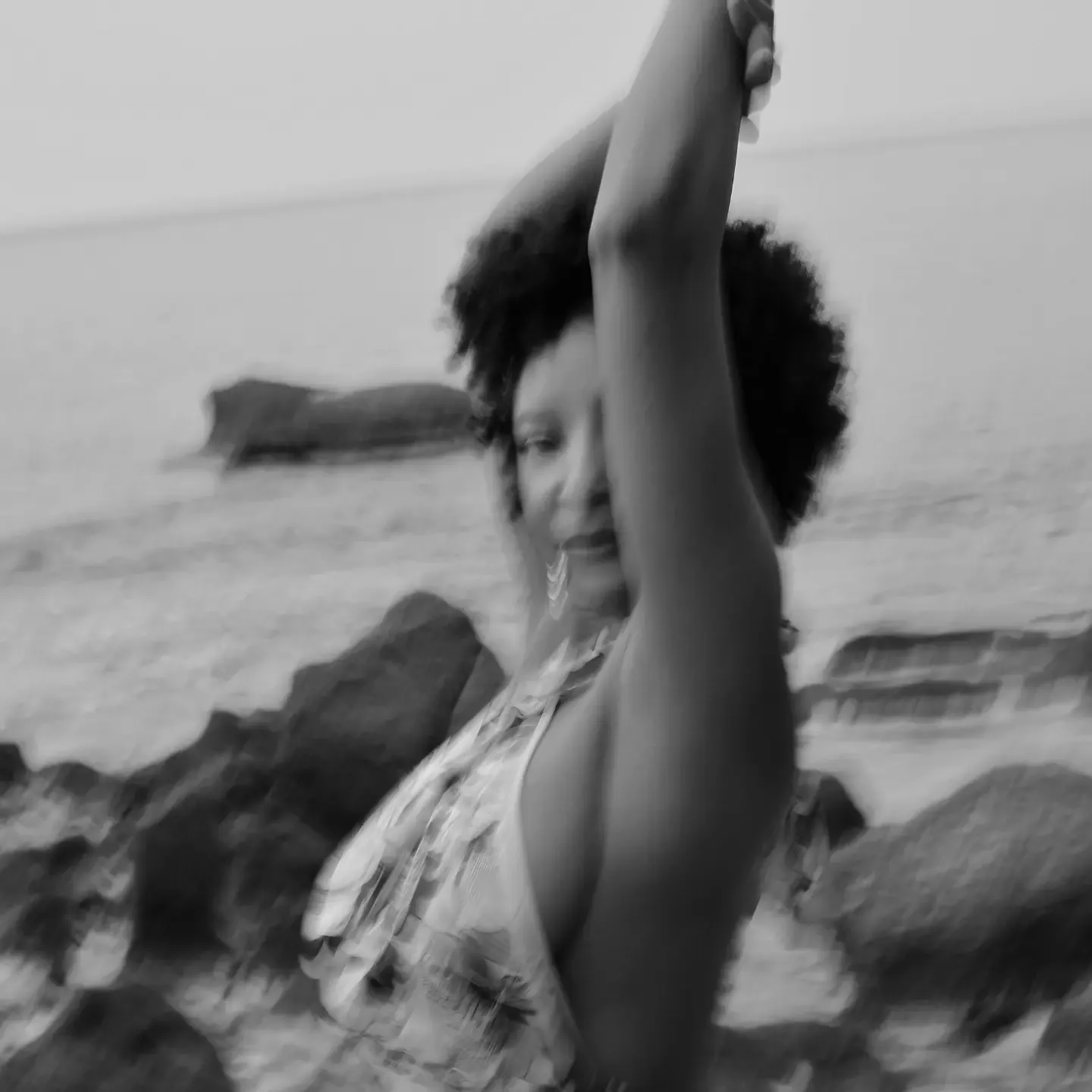 A woman outside near a lake, exploring a range of motion with her arm raised.