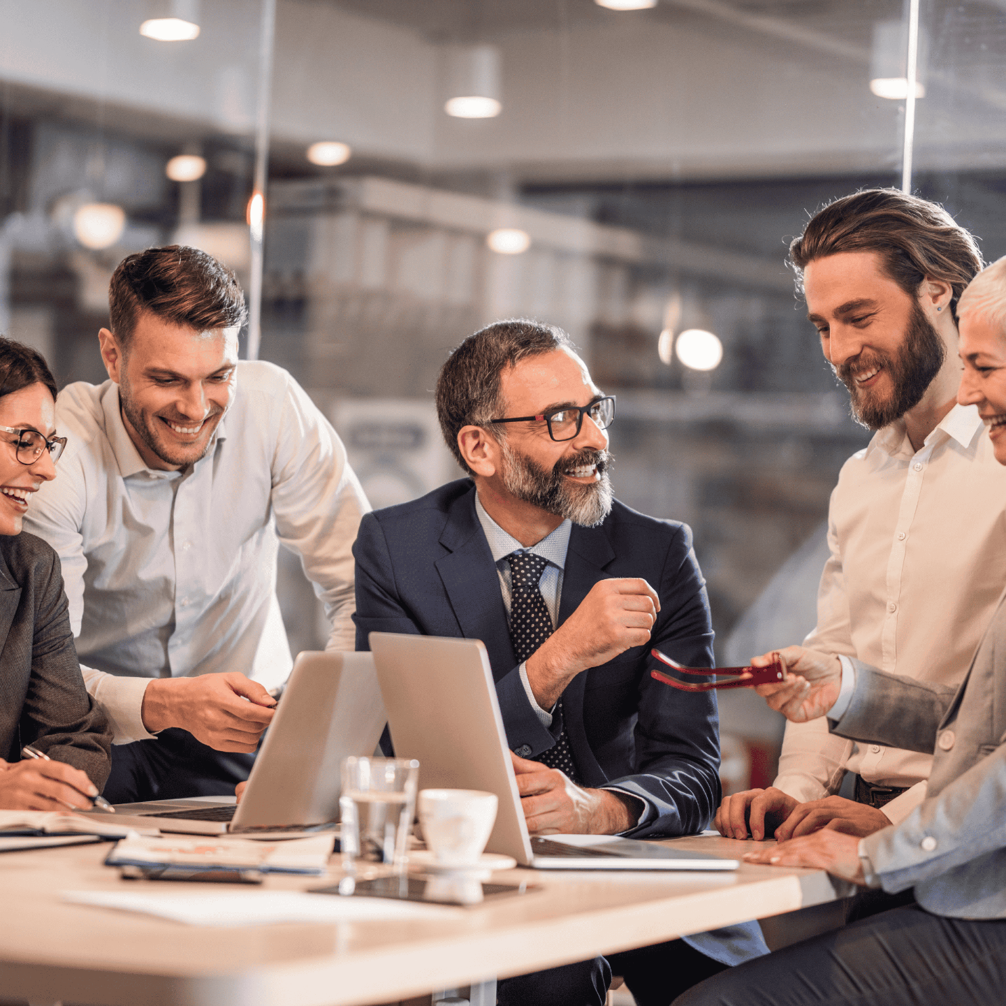 Five people standing around a table with two computers smiling at each other.