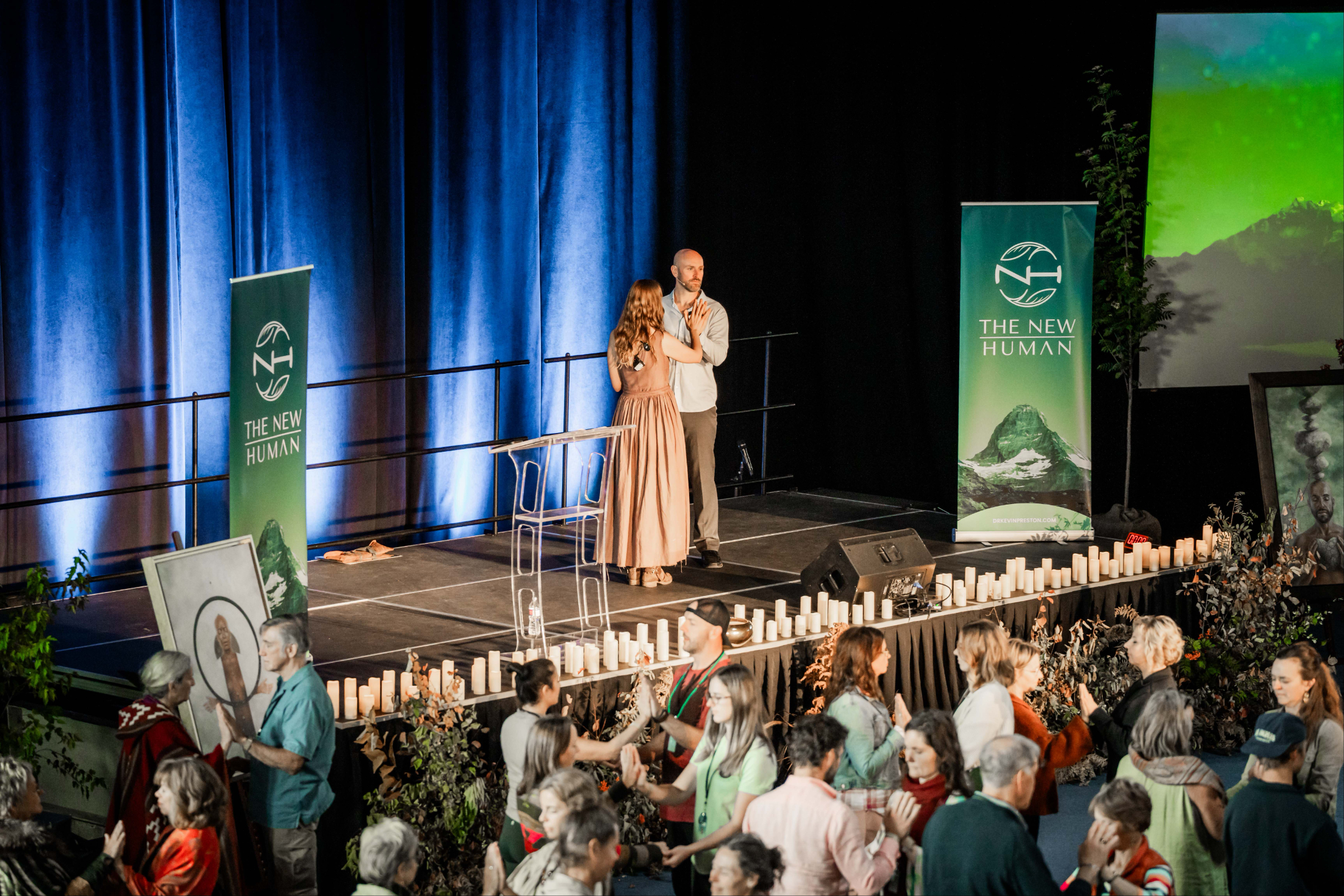 Courtney and Mike on stage at New Human Conference looking over audience leading a partner activity