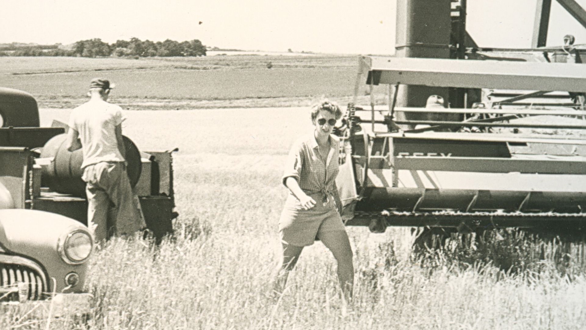 woman walking with sunglasses in a wheat field by farm equipment