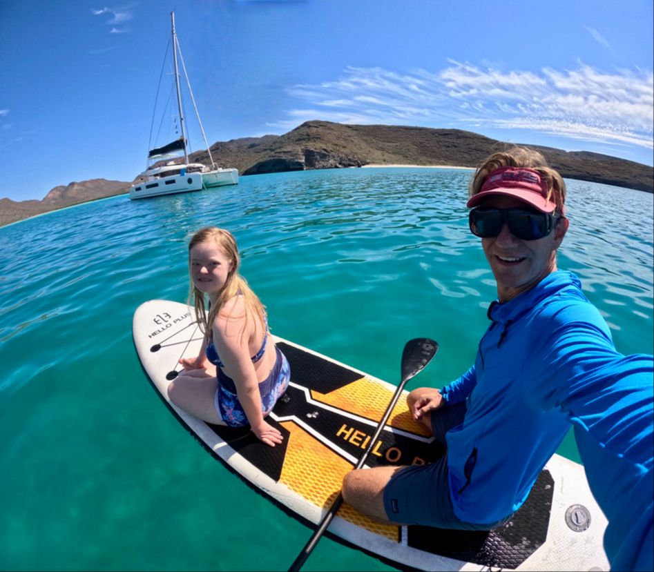 Father and daughter with Down Syndrome on a paddle board with a sailboat