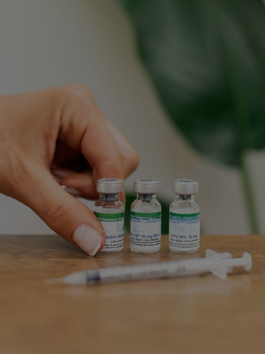 Hand holding on to one of three vials and an injection on a table