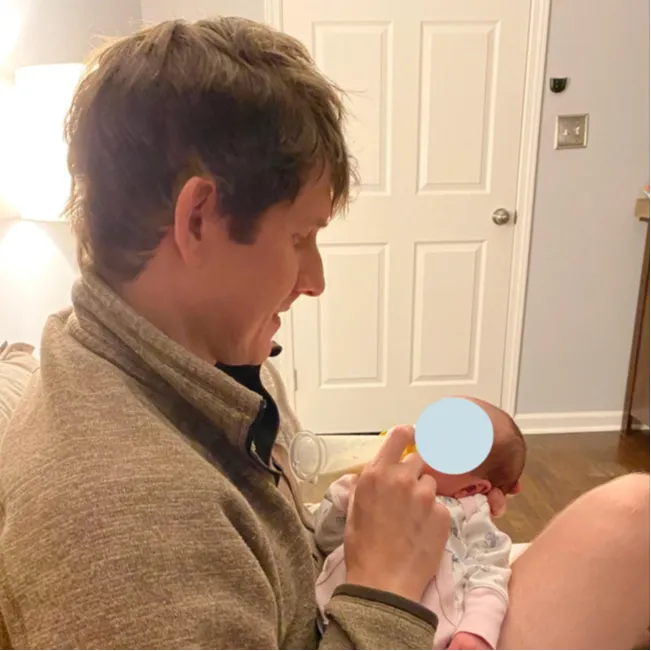 Dad sitting down on bed feeding newborn baby a bottle
