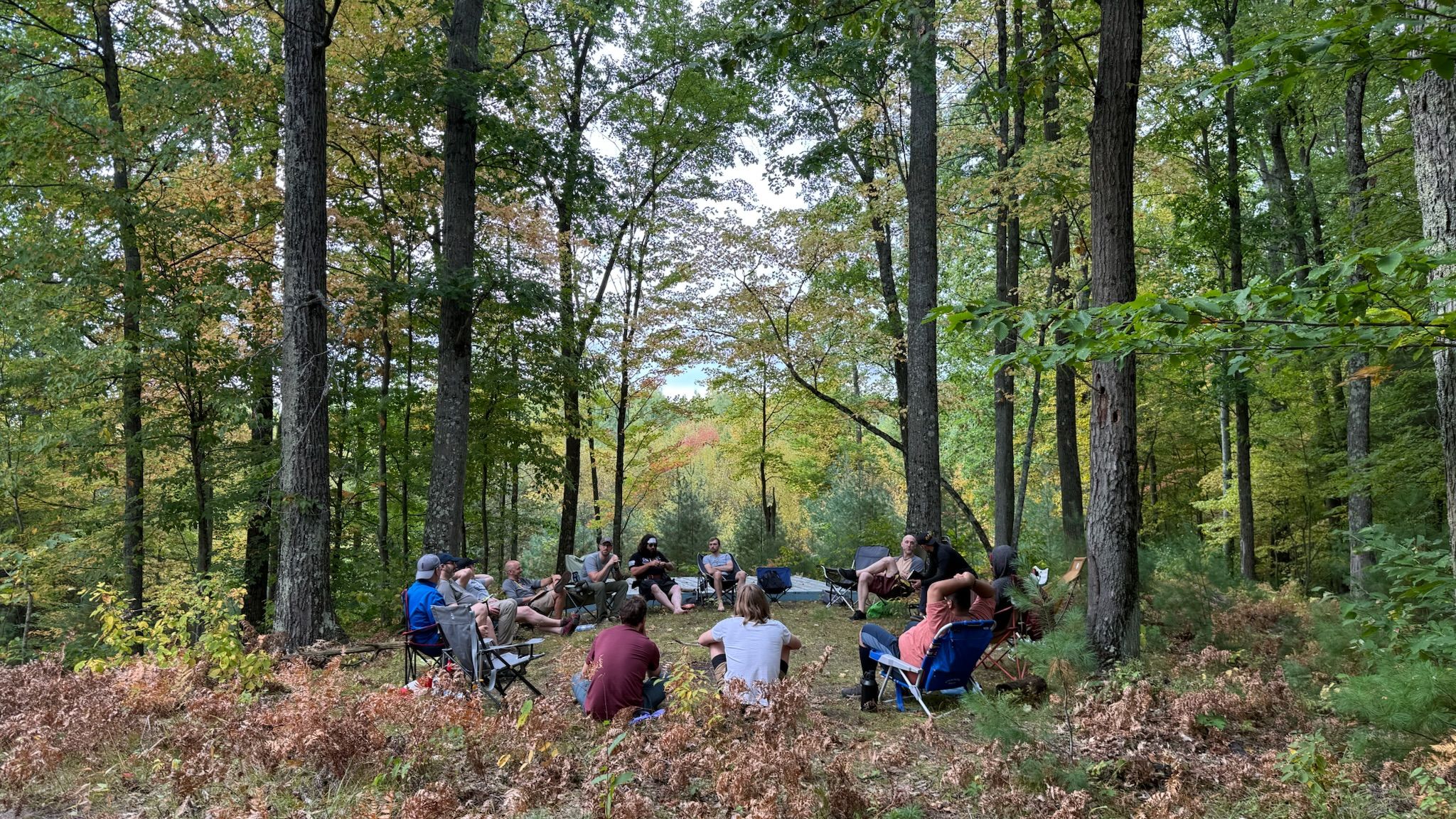 A group of men sitting in a circle in the forest during a facilitated session at a past Metro-Detroit Men's Therapy retreat in northern Michigan