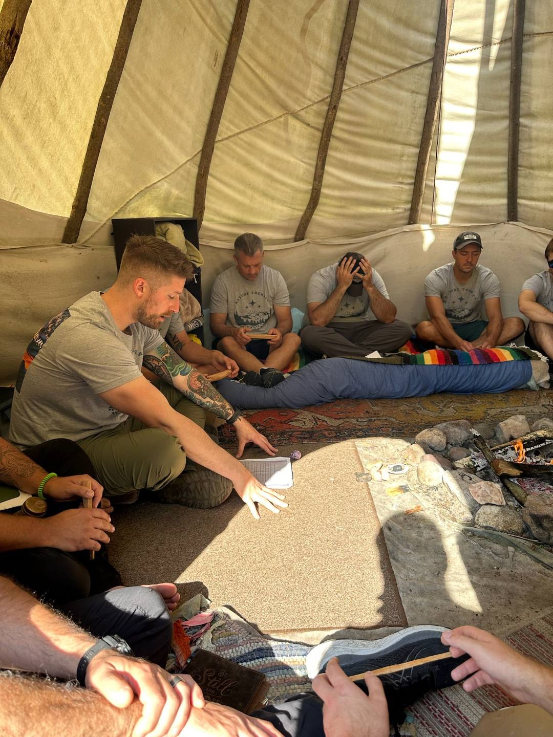 Men sitting in a circle inside a tipi during a deep work session at a Metro-Detroit Men's Therapy retreat in Michigan