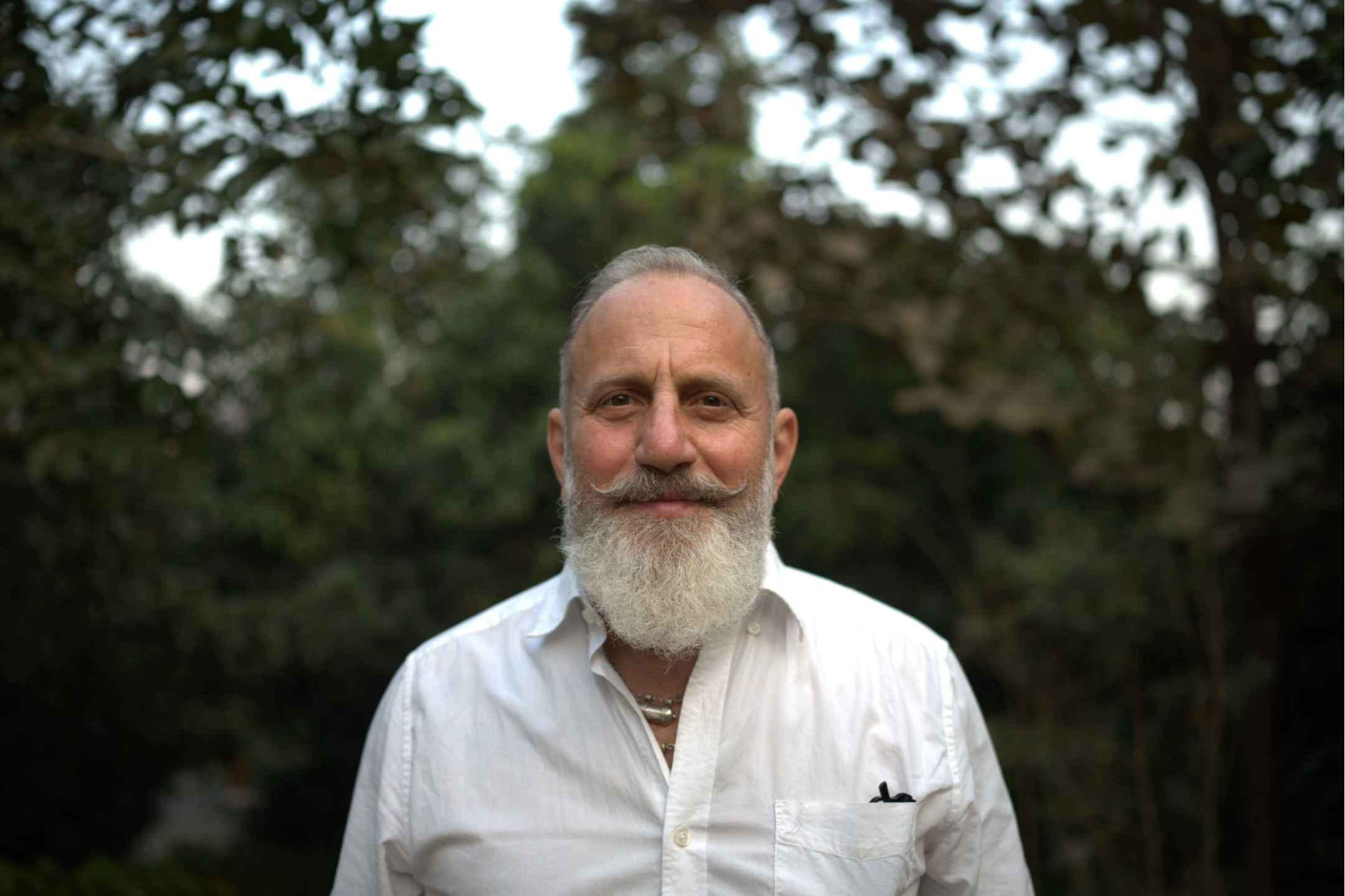 Portrait of Raghunath, founder of Kirtan School, standing outdoors in a white shirt with greenery in the background.