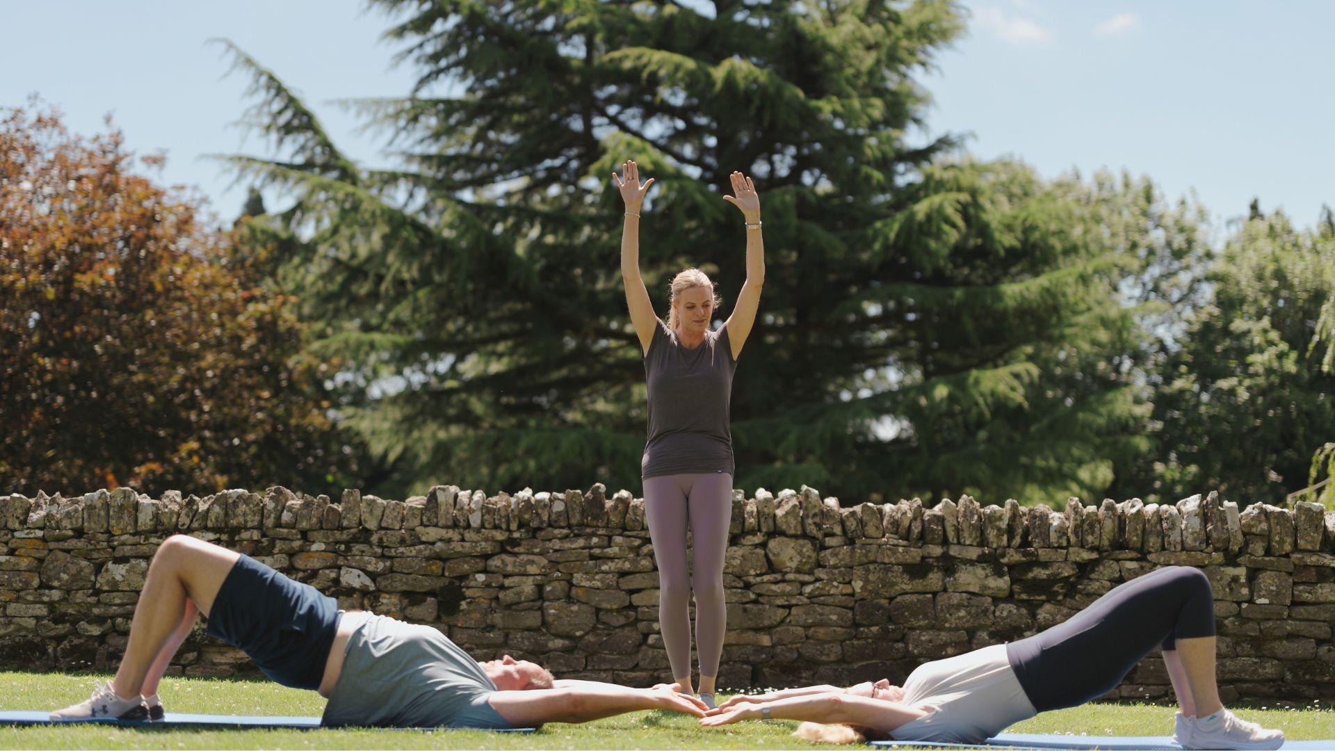 Kari Sherman coaching a man and woman through a spine curl with rib cage closure in a beautiful garden setting.