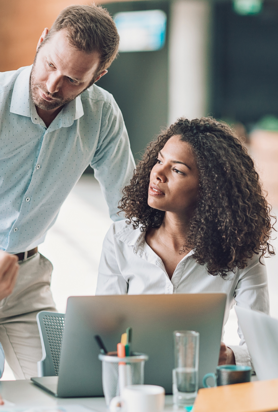 Two professionals in an office listening to another colleague