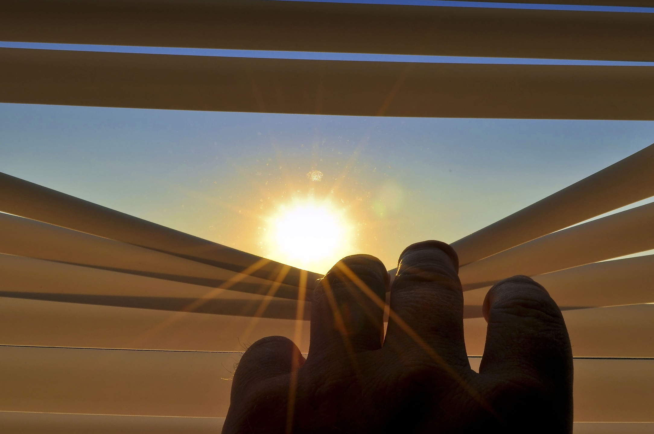 hand opening horizontal blinds to a sun
