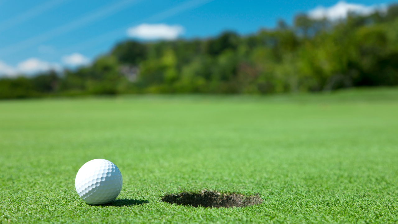 Golf ball on the green sitting next to hole. 