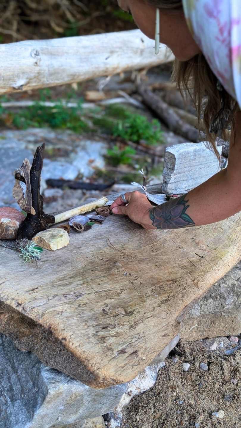 Person creating an altar with feathers and stone on a fallen tree on a beach