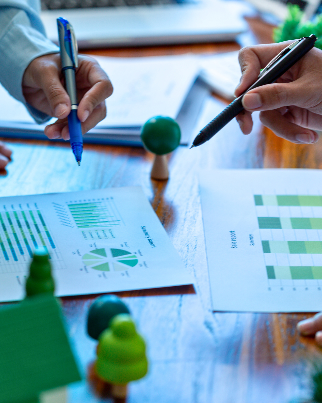 Two professionals holding pens reviewing sustainability reporting data on charts