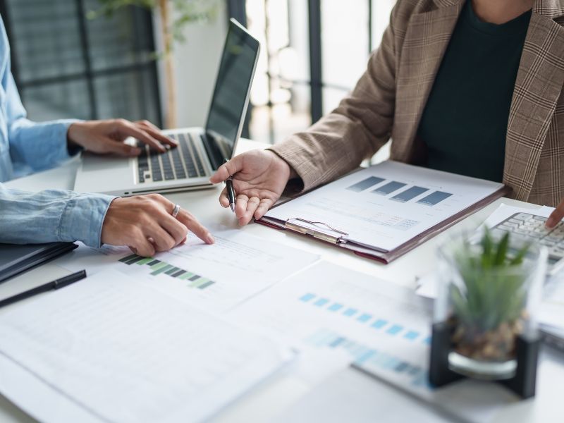 Two people meeting at a table with charts and a laptop computer in front of them