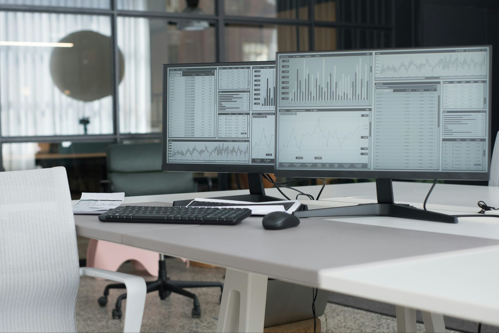 Professional workstation shows two computer monitors with general analytics on the screen. In the background is a closed office.