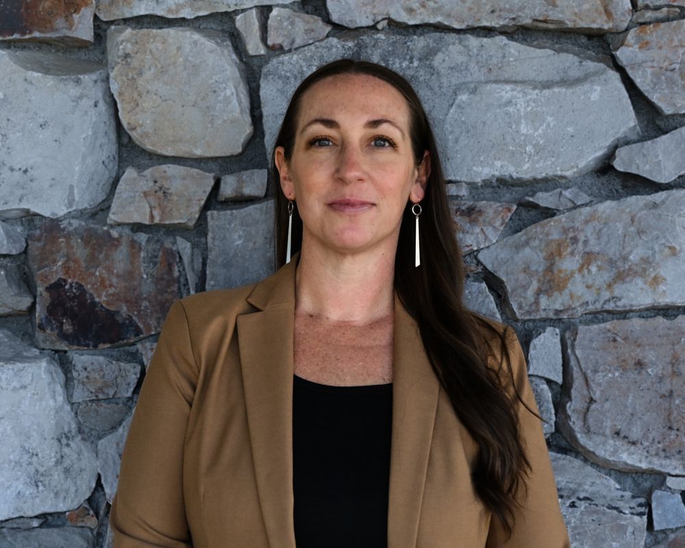 Jill Klott standing in front of stone wall wearing tan blazer