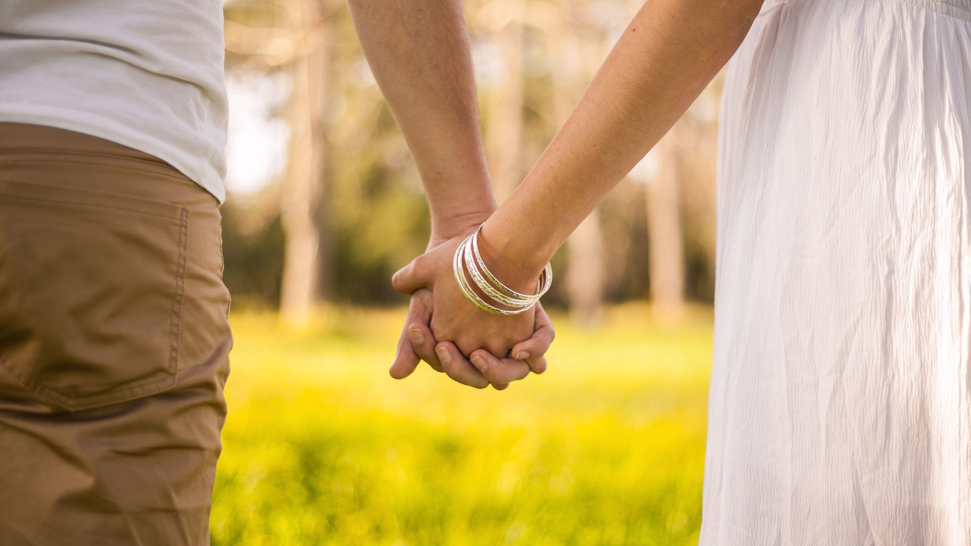 Gros plan de deux mains qui se tiennent fermement dans un champ ensoleillé, représentant le lien solide et l'engagement du couple.