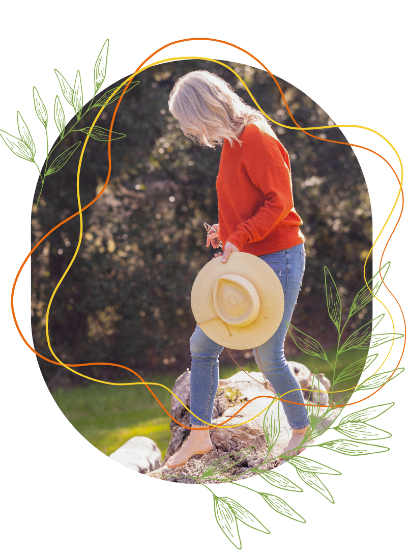 Kathleen with long gray hair smiles at the camera, wearing a mustard yellow sweater and a necklace, with abstract graphic lines and leaves in the background, reflecting her deep connection to nature education.