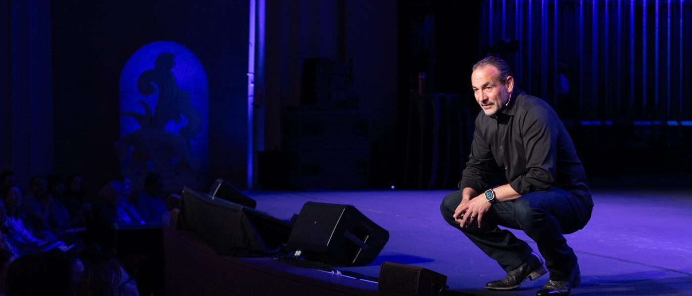 Mel Abraham kneeling on stage connecting with his audience