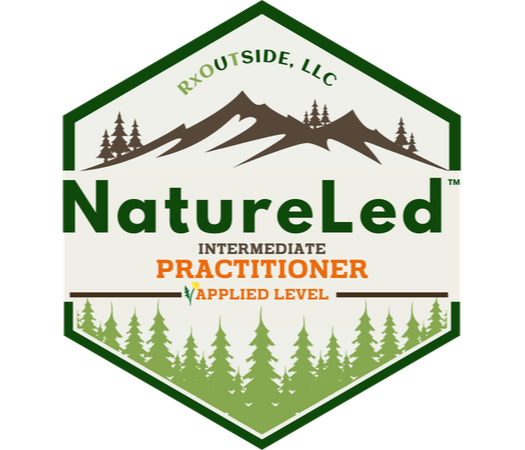 A smiling Kathleen with long gray hair wearing a maroon jacket and necklace stands before a backdrop adorned with green leaf illustrations, embodying the joy of nature connection.