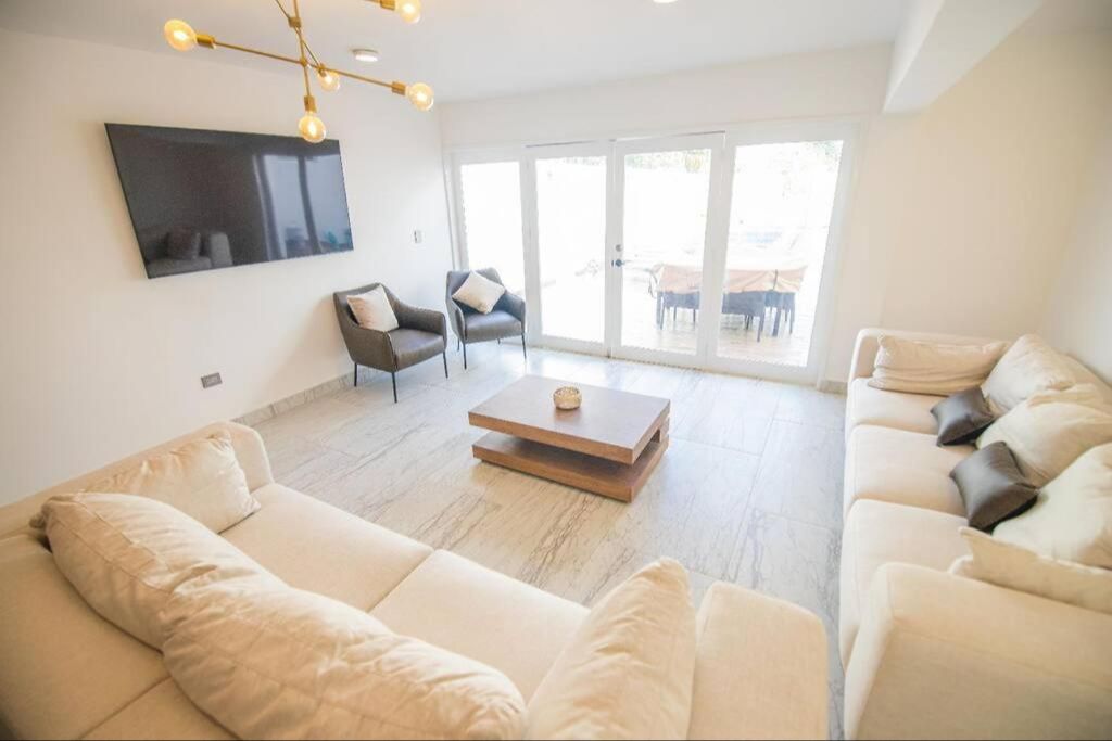 Brightly lit living room with 2 large comfortable looking couches facing a large TV on the wall.