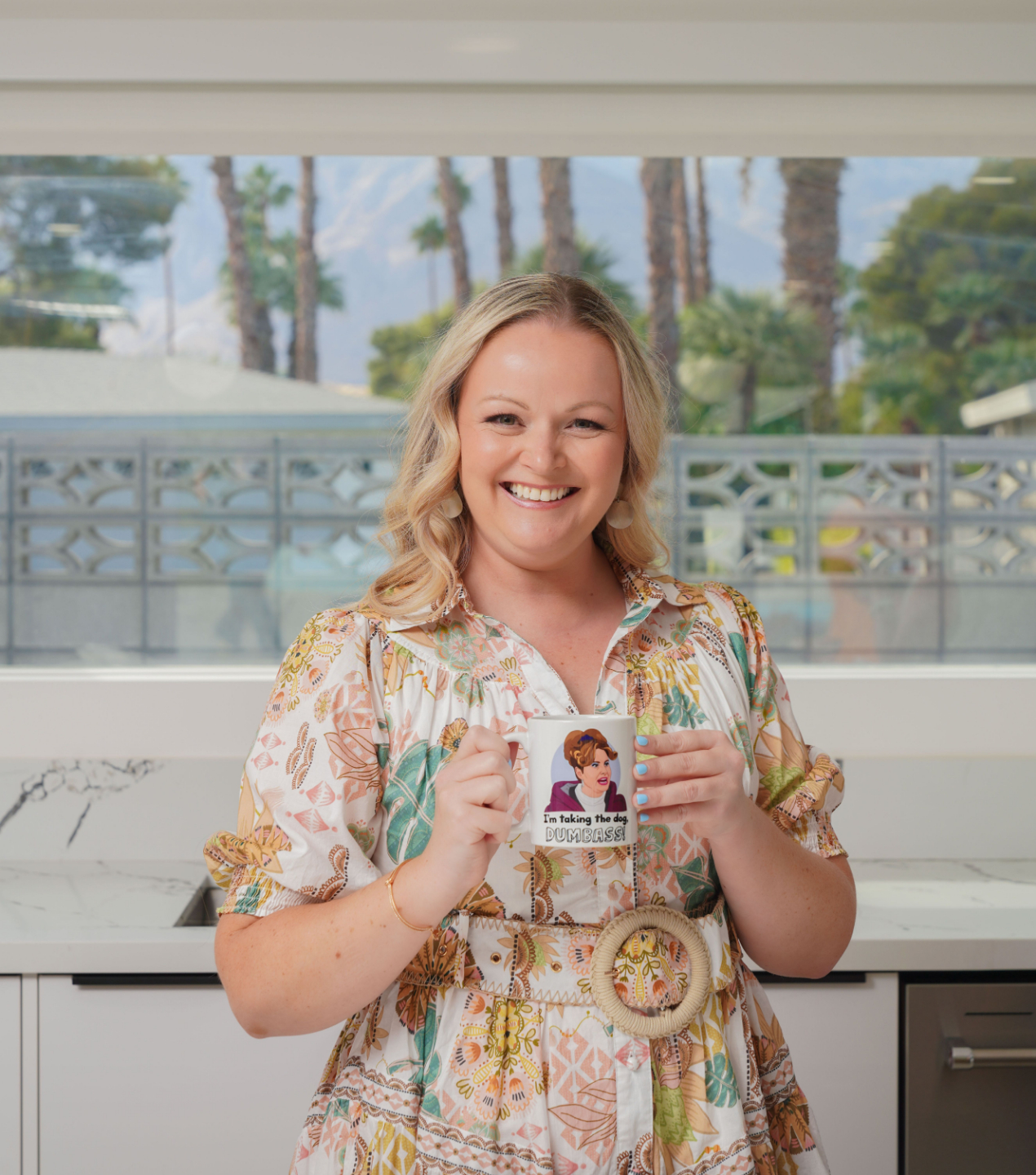 Stacy Munzenberger in a floral dress holding a cup