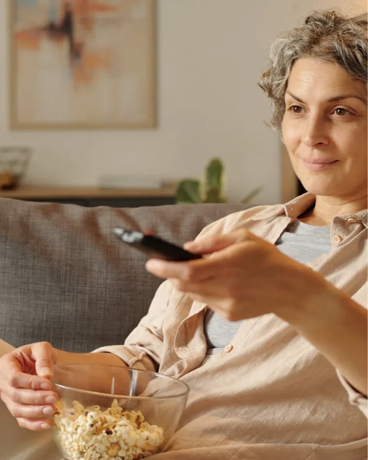Woman relaxing on couch eating popcorn and watching TV at home