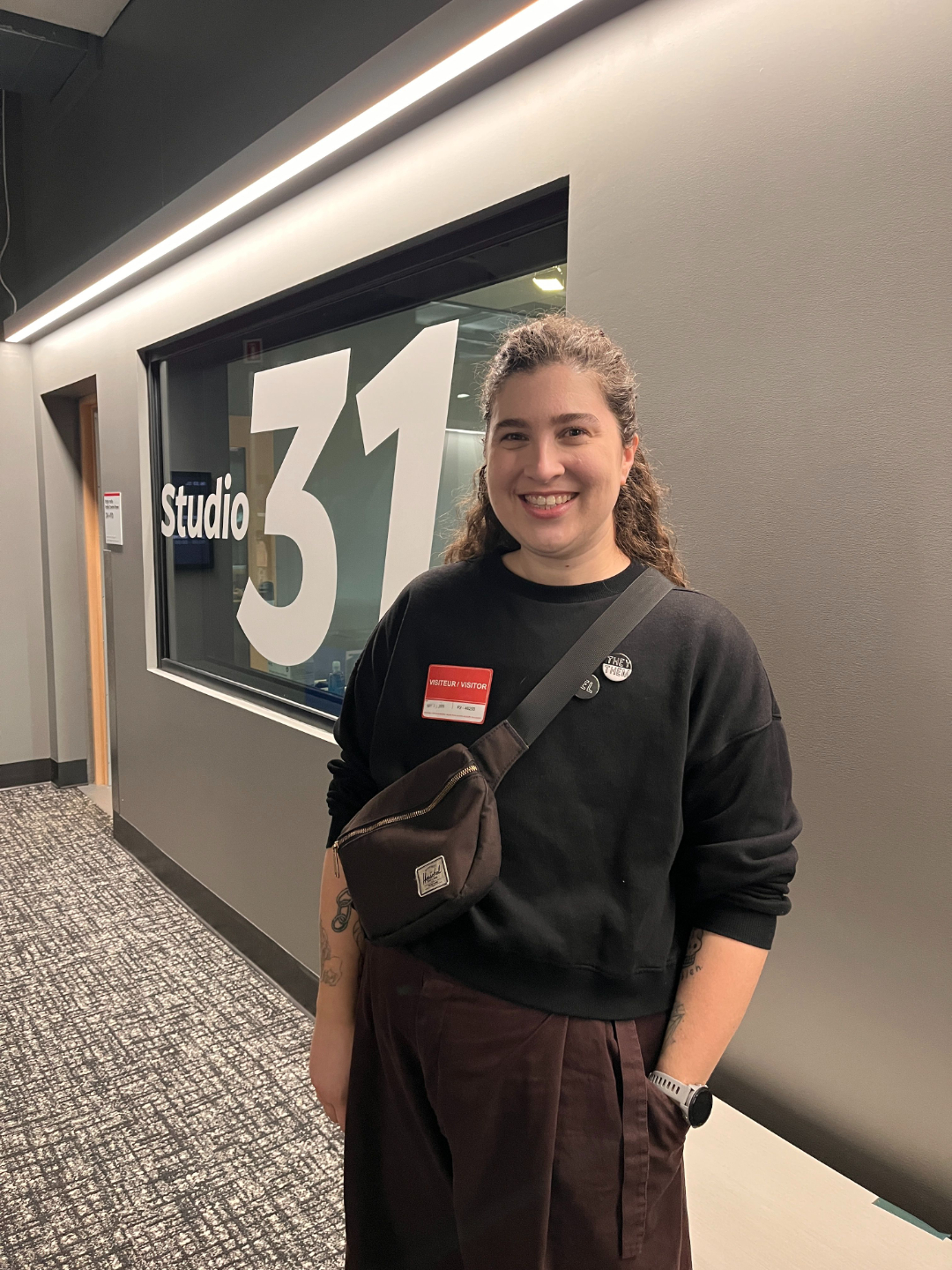 Ren&eacute;e Yoxon smiling outside CBC Montreal's Studio 31, wearing a visitor badge and they/them pronoun pins