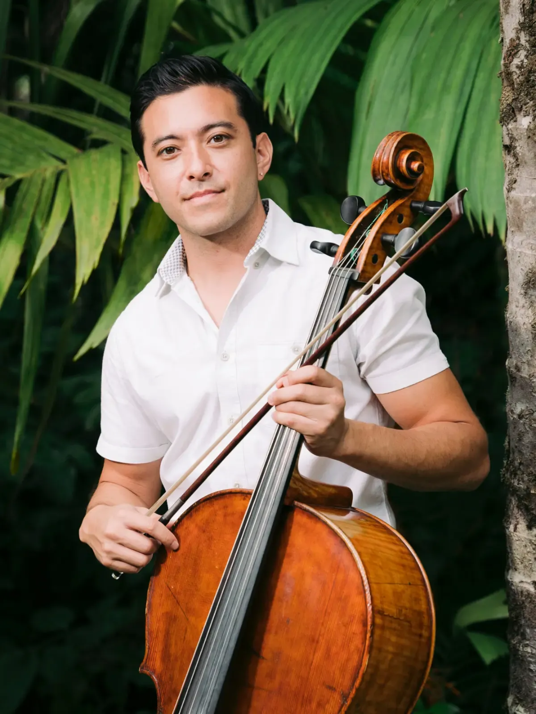 Josh Nakazawa playing cello surrounded by tropical Hawaiian greenery