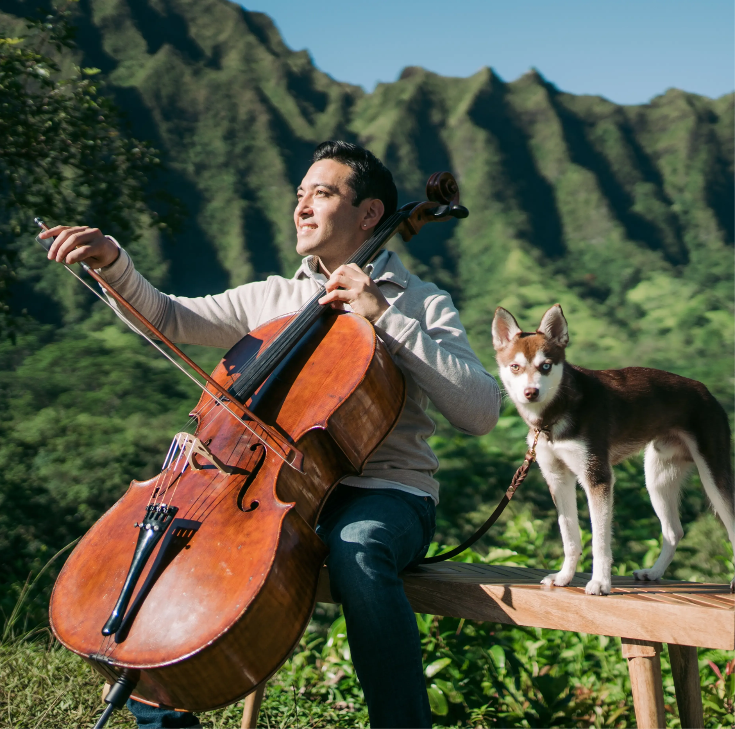 Josh Nakazawa playing cello in front of the Ko'olau mountains with his dog