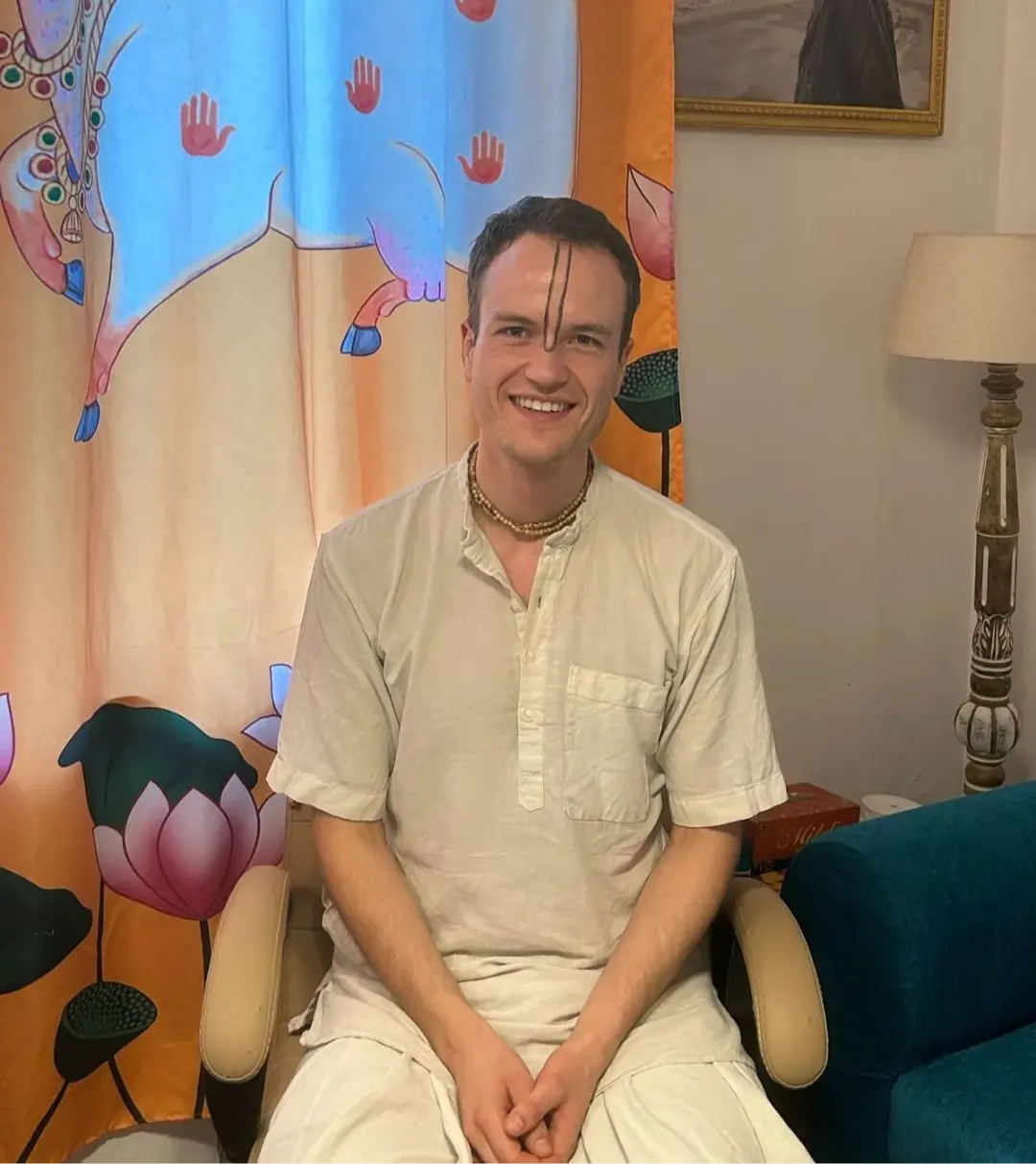 A smiling student sitting in front of a colorful tapestry, sharing a testimonial about their personal growth and breakthroughs.