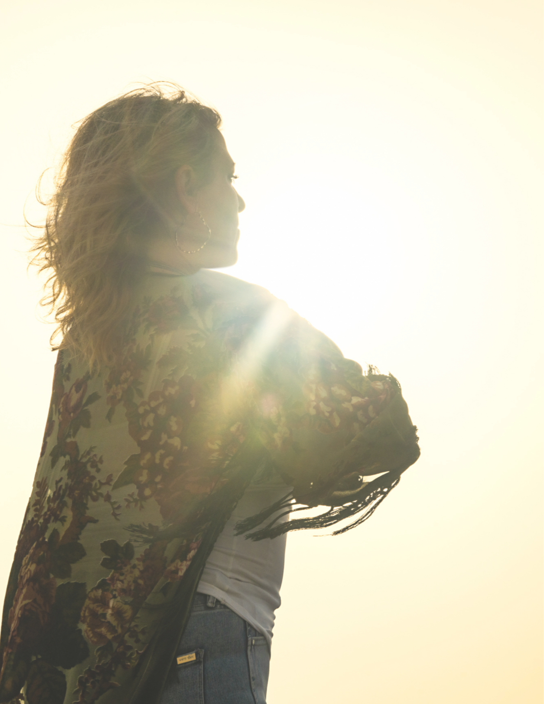Woman hands wide open on rocks with ocean and sun