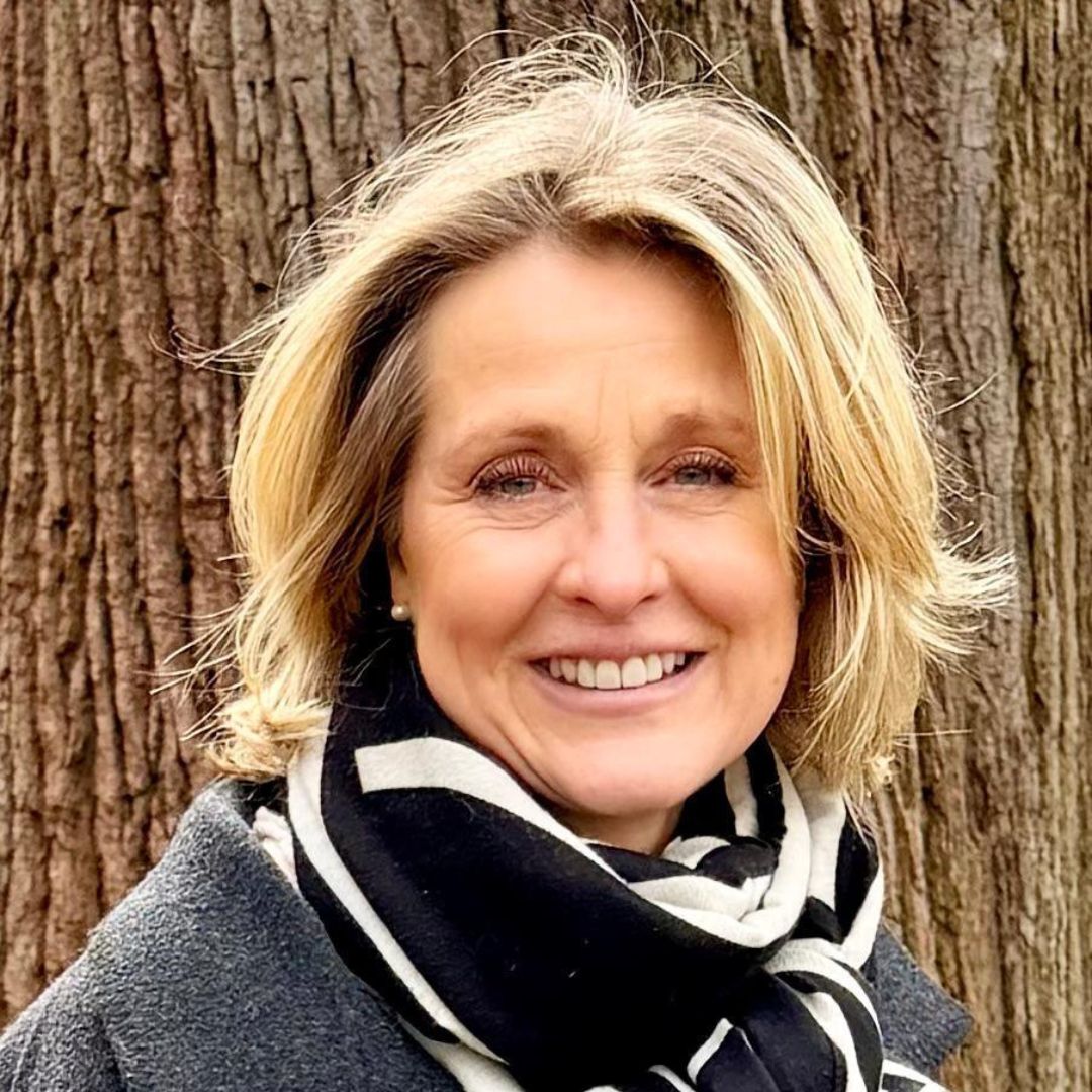 Smiling mature blonde woman with a black and white scarf standing in front of a tree