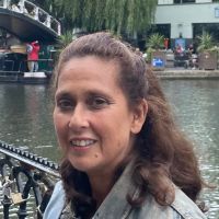 smiling mature woman with tied back long brown hair and a river in the background
