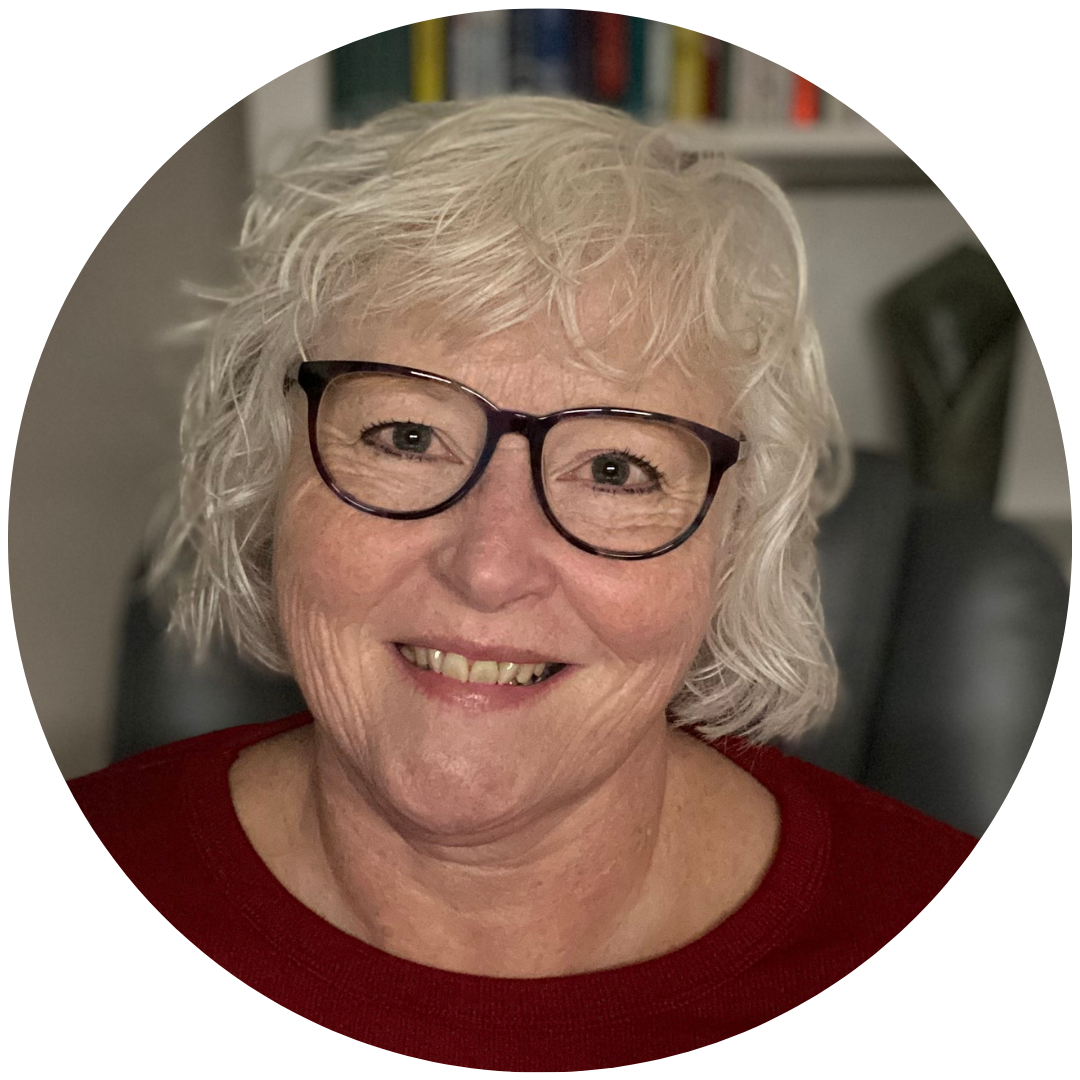 Helen, a 58 year old smiling woman with shortish wavy white hair and glasses in a red top with a blurred bookcase in the background.