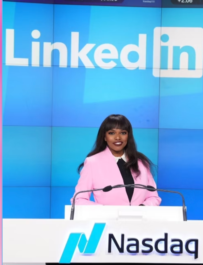 Katheline Jean-Pierre stands at a Nasdaq podium with microphones, wearing a pink blazer, in front of a blue LinkedIn-branded backdrop.