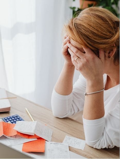 woman sitting at desk with calculator and papers in front of her and her hands are holding her head