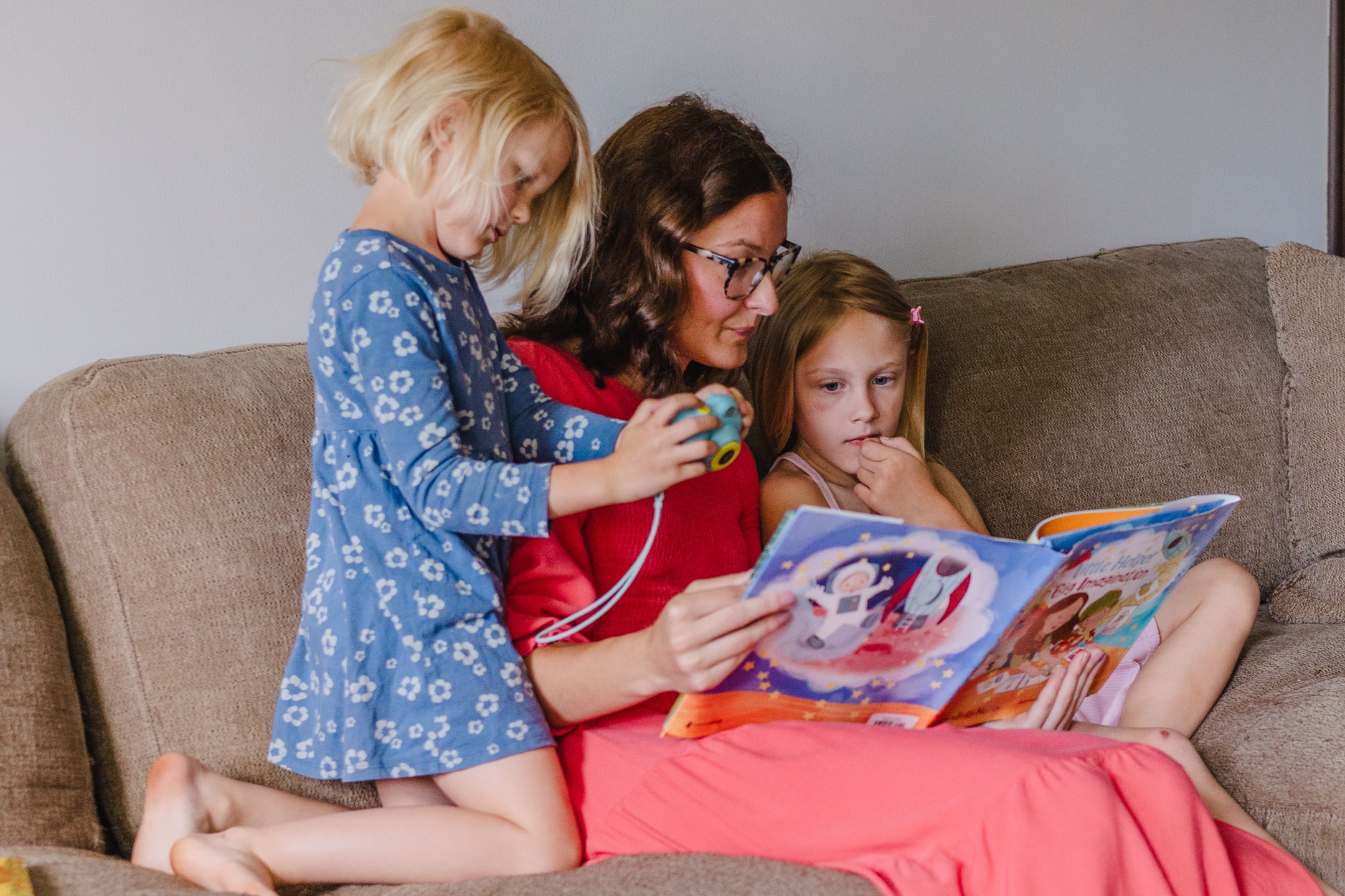 A mother reading with her two daughters on the couch.