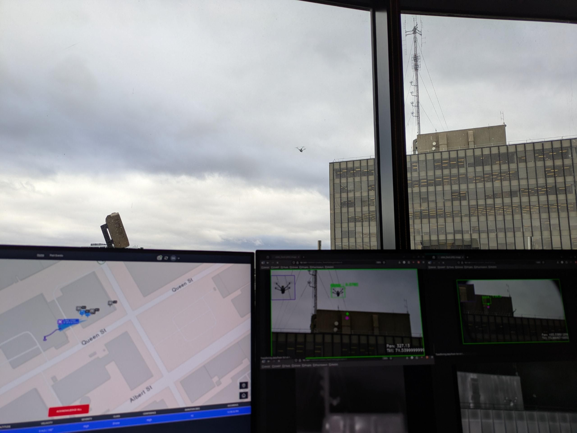 Three computers showing a command-and-control interface for counter-drone operations, with a drone in the sky behind them.