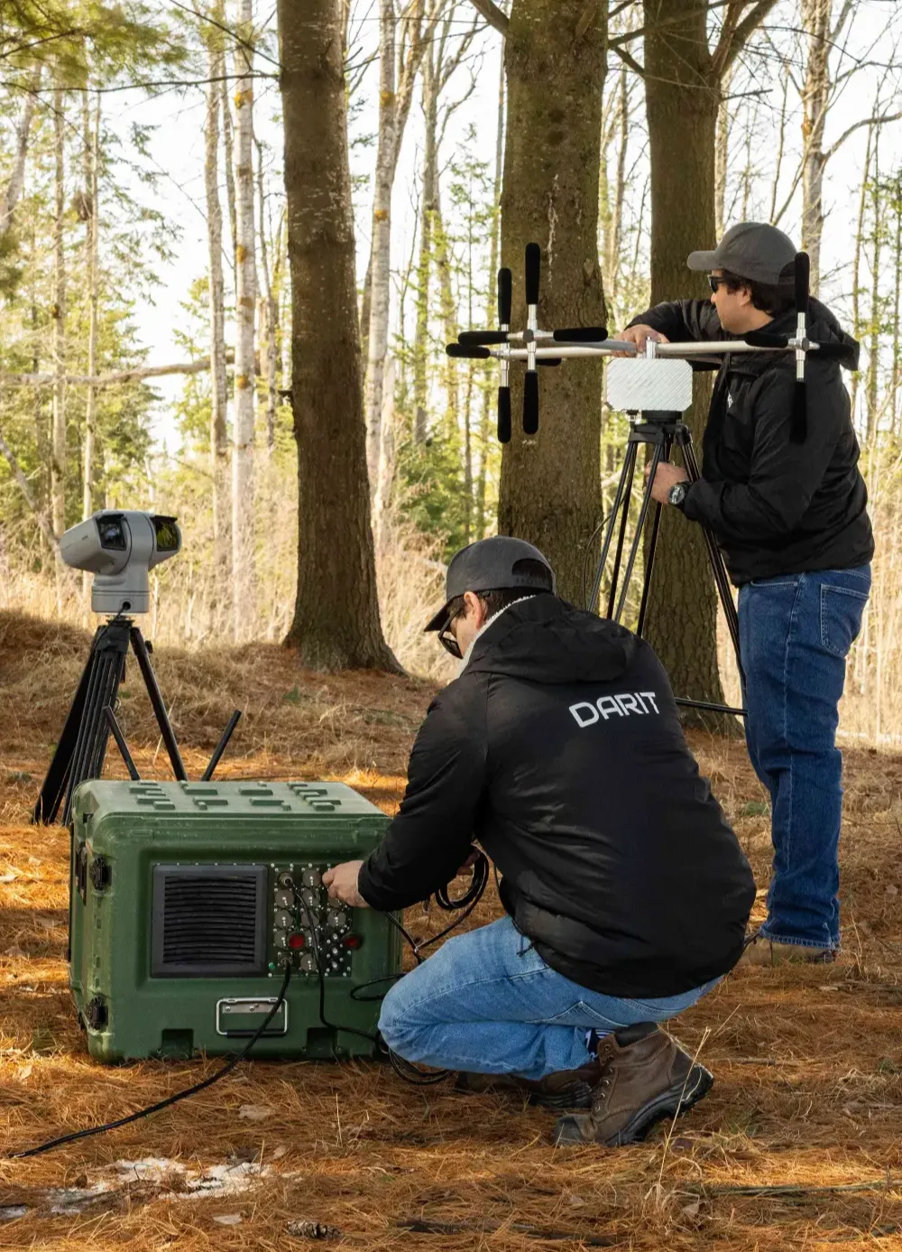 Two technicians deploying a counter‑drone sensor station in a forest environment