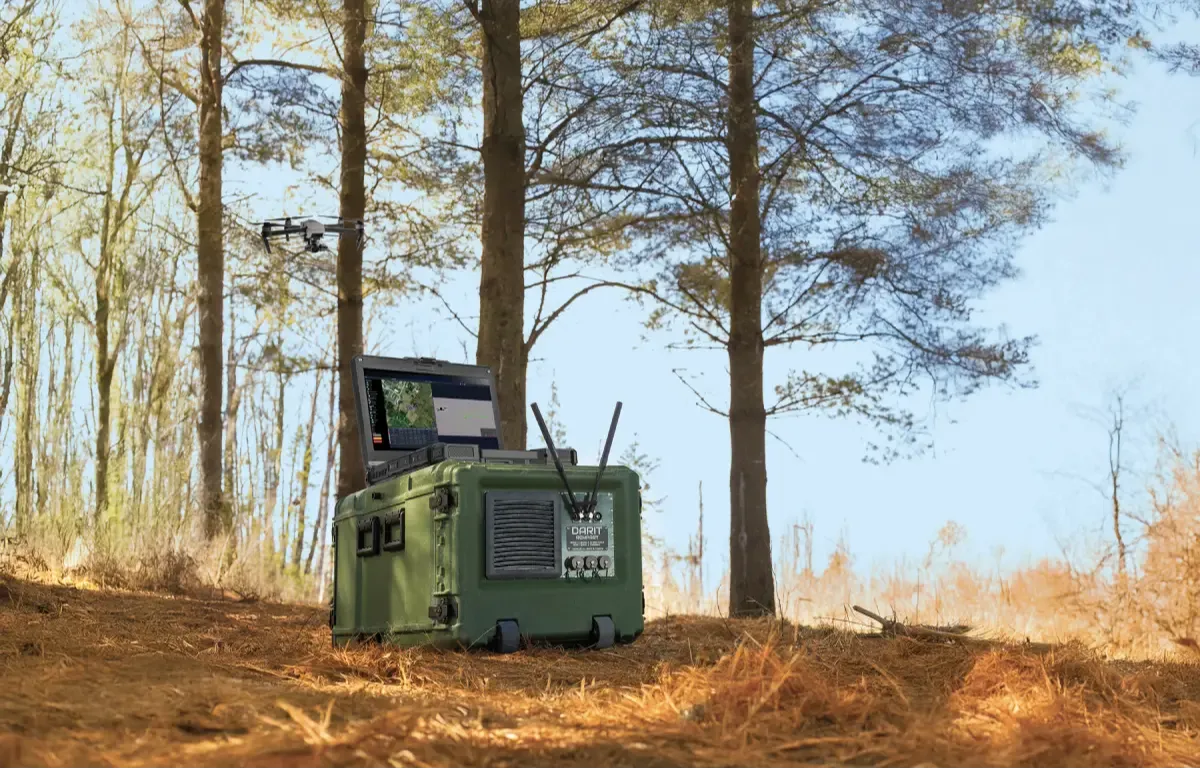 Unité de commandement et contrôle déployée sur le terrain, équipée d’antennes et d’un écran, assurant la surveillance d’un drone à proximité dans un environnement extérieur boisé