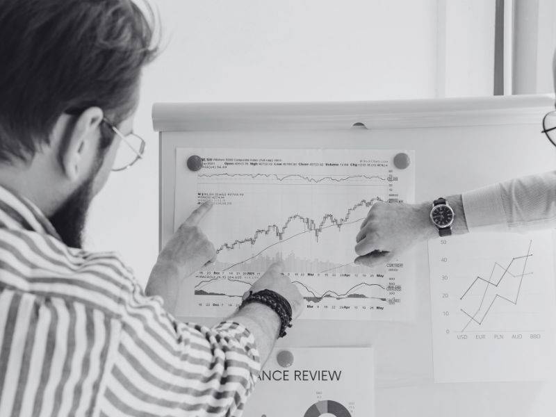 two people pointing to financial charts displayed on a whiteboard